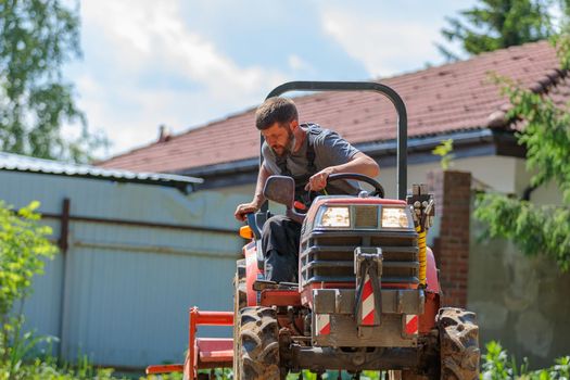 A man on a mini-excavator levels a piece of land, loosens the soil