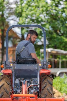 A man on a mini-excavator levels a piece of land, loosens the soil