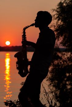 Silhouette of a young guy playing the saxophone in the evening at sunset.