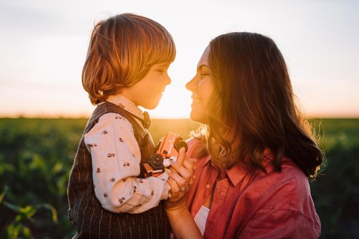 Tender scene of loving son with mom on sunset backdrop. Beautiful family. Cute 3 year old kid with mother. Parenthood, childhood, happiness, children wellbeing concept. High quality photo