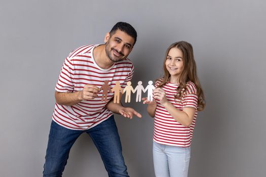 Portrait of father and daughter in striped T-shirts holding paper chain multiracial people, symbol of community, unity, people and support. Indoor studio shot isolated on gray background.