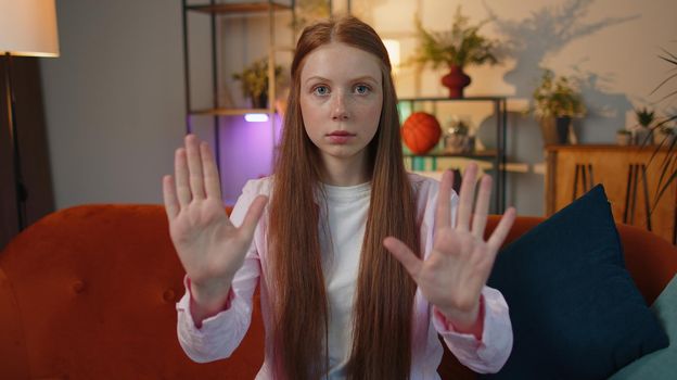 Stop gesture. Angry redhead child girl say No hold palm folded crossed hands, warning of finish, prohibited access, declining communication, body language, danger. Kid at home room apartment indoors