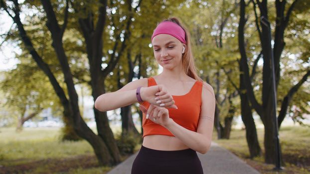 Athletic runner girl look at smart watch clock device fitness bracelet checking time, heart rate, pulse, SPO2 on smartwatch on jogging. Woman workout cardio training outside in city park at morning