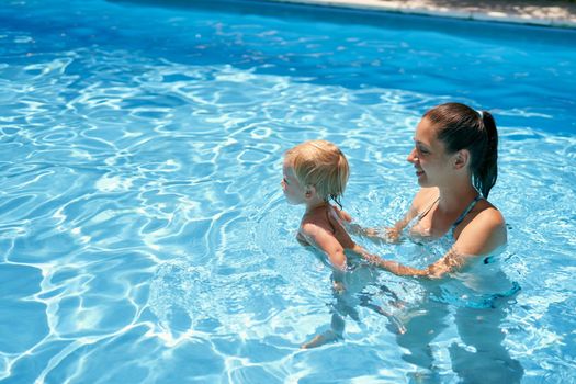 Mom teaches a small baby to swim in a pool with turquoise water. High quality photo