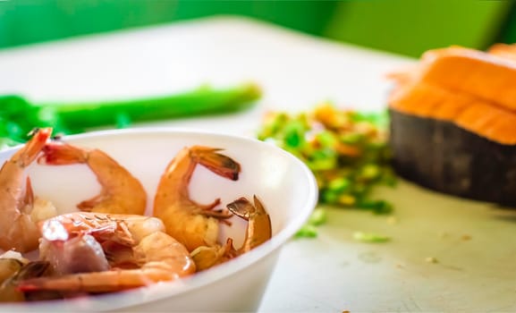 Bowl of raw shrimp on the table with vegetables out of focus background, Raw shrimp on the table with vegetables out of focus background