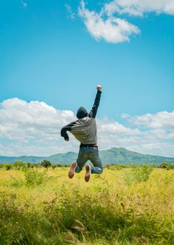 Rear view of man jumping in the grass raising fist, Concept of a free person jumping and raising his arm, Free person jumping with happiness in the field, man from back jumping in a nice field
