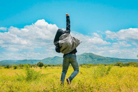 Man from back jumping in a nice field, Rear view of man jumping in the grass raising fist, Concept of a free person jumping and raising his arm, Free person jumping from back in the field