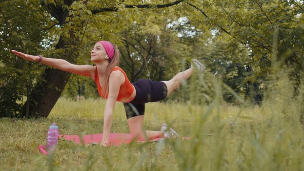 Athletic sporty fit girl doing workout in park on sport mat performing training yoga pilates. Plank pose. Raises legs and hands. Young woman enjoying exercising outdoors. Active sportswoman motivation