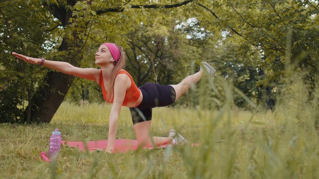 Athletic sporty fit girl doing workout in park on sport mat performing training yoga pilates. Plank pose. Raises legs and hands. Young woman enjoying exercising outdoors. Active sportswoman motivation