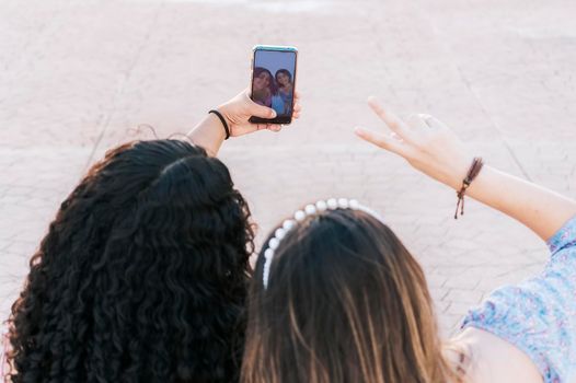 Two smiling teenage girl friends taking a selfie and pointing fingers up. Close up of two smiling teenage girlfriends sitting taking a selfie