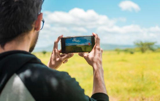 Rear view of a person taking a photo of a field with his cell phone, rear view of a man taking photos of a field, Close up of tourist man taking photos of a landscape.