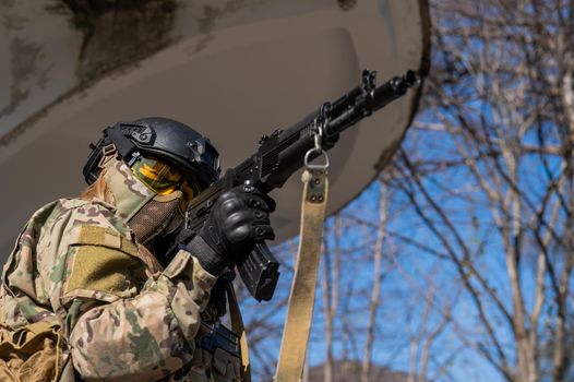 Portrait of a woman in a helmet and goggles with a machine gun in her hands. A female soldier in a camouflage uniform holds a weapon