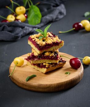 Square slices of cherry crumble lie in a stack on a black background	
