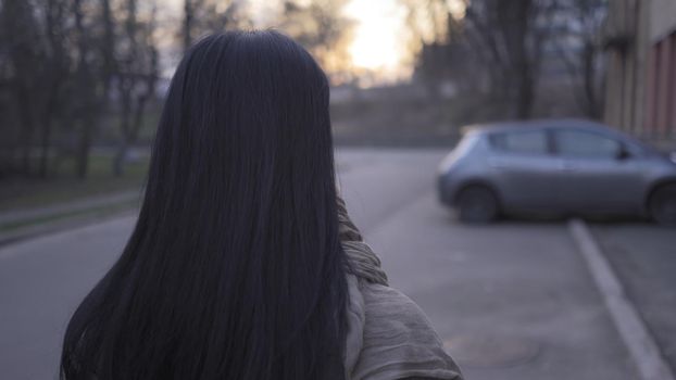 Brunette Admires The Sunset While Standing On Deserted City Street Near Parked Cars, Rear View Of Single Woman In Evening During Quarantine Due To Virus Outbreak