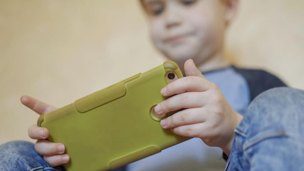 Child Uses Mobile Phone Playing Or Learning, Caucasian Boy In Casual Wear Spends Time Using Smart Phone At Home, The Boy Needs To Stay At Home Due To Quarantine, Close Up