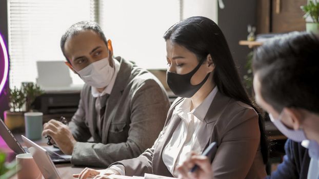 Teamwork Of Business People During Virus Outbreak, Colleagues In Protective Masks Working In Office, Selective Focus On Beauty Asian Woman Using Laptop