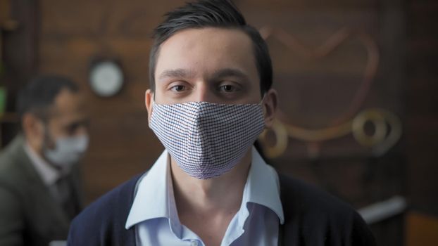 Serious Businessman In Protective Mask, Portrait Of Caucasian Office Worker Working In Office During Pandemic, His Colleague Working On Blurred Background