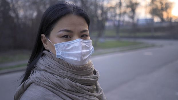 Woman In Protective Mask Stands On Empty City Street In Sunset Background Outdoors Looking At Camera, The Quarantined Country At COVID 19 Pandemic