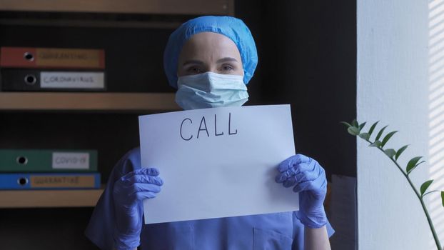 Medic In Protective Uniform Shows Slogan to Make Call, Young Woman Demonstrates Inscription On Piece Of Paper Standing Near Window In His Office, Healthcare Concept