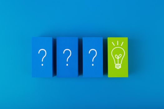 Creative concept of brainstorming, creativity and fresh ideas. Flat lay with blue blocks with drawn questions and green with light bulb on blue background