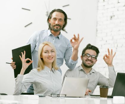 OK gesture from a friendly company of colleagues sitting at the office table, smiling employees show OK gestures while sitting In a bright and comfortable office. Toned image.