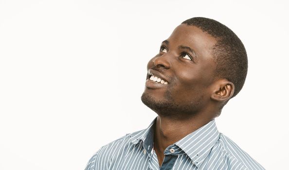 African american handsome man toothy smiles looking up and to the side, Dark-skinned young guy in blue striped shirt isolated on white background. Copy space located at left side. Toned image.