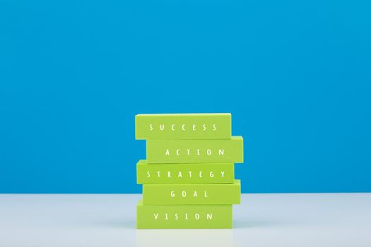 Business success or development trendy modern bright concept. Stack of green tablets with text vision, goal, strategy, action, success against blue background. Colorful scoring a goal concept