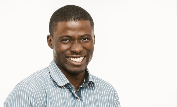 Handsome African guy with white-toothed smile looking at camera, dark-skinned well-dressed young man cut out on white background. Concept of dental care. Copy space at right. Toned image.