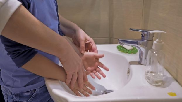 Mom Helps Her Little Son Wash The Hands Correctly, Female Hands Hold Children's Hands Over The Washbasin, Close Up Shot, Hygiene Rules Concept