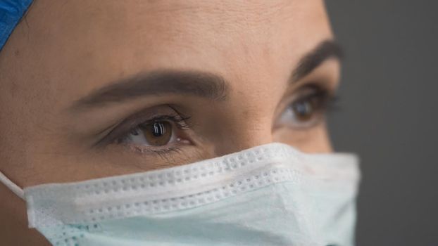 Portrait Of Medic In Protective Mask And Blue Cap Looking At Side, Selective Focus On Left Eye, Close Up Of Doctor's Eyes, Half Turn View, Pandemic Concept