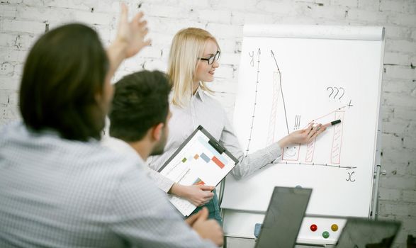 Female speaker presents business development charts, business woman shows schemes hanging on a white board, a friendly team of employees is involved in the discussion. Toned image.