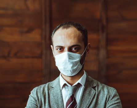 Well-Dressed Man In Protective Mask Looks At Camera, White Collar Male Worker Or Boss Standing In Deserted Office Alone During Quarantine Due To Epidemic Of Coronavirus