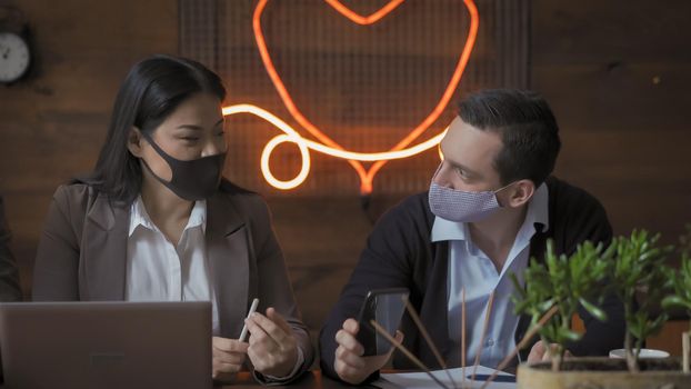 Business People Communicate While Observing The Distance During Coronavirus Epidemic, Coworkers In Protective Masks Work In Modern Office With Neon Lights And Beautiful Wooden Wall, Pandemic Concept