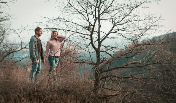 Happy Man and Woman dating in nature. Couple of young people in love stands holding hands while admiring the natural landscape. Adventure and travel concept.