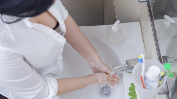 Woman Washing Her Hands With Antibacterial Soap, Sexy Brunette Washes Soap Foam From Her Hands Bending Over A White Washbasin In The Bathroom, High Angle View