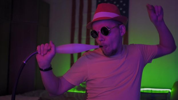 Hipsters Having Fun Self-Isolation Time, Caucasian Man Wearing Safety Sunglasses Dancing And Smoking Hookah At Home During Quarantine On USA Flag Background, Cheerful Quarantine Concept