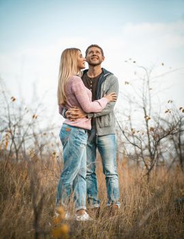 Couple In Love Is Standing In Embrace Enjoying The Autumn Nature, Young Caucasian Man Raised His Face To Sky Hugging Woman, Two Tourists Standing On Grass Outdoors, Blue Sky On Background, Full Length