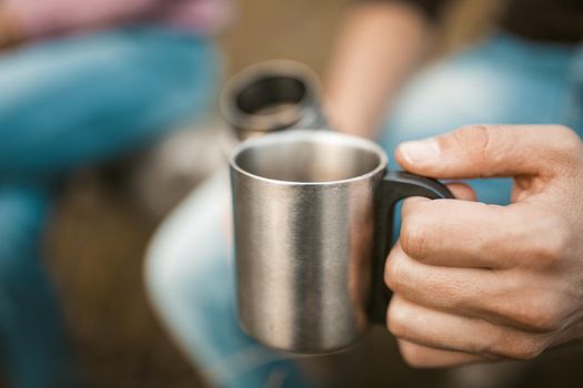 Males Hand Holding Metal Cup With Hot Drink, Caucasian Man And Woman Have Coffee Break Sitting On Fallen Trunk Of Tree Outdoors, Close Up Shot