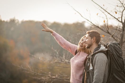 Tourists In Love Admire Sunset On Edge Of Cliff Outdoors, Laughing Blonde Reached Out To The Sunshine, Selective Focus On Caucasian Man With Large Backpack Looking Into The Distance