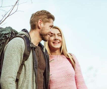 Couple of tourists smiling while stands embracing against a blue sky. Selective focus on Profile view of Caucasian young man with big backpack. Travel concept.