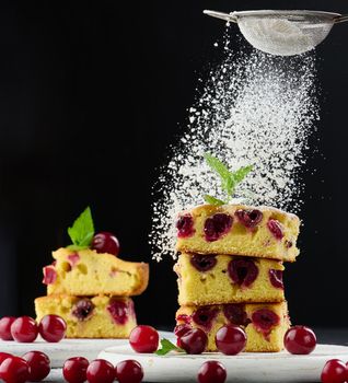 Baked sponge cake with cherries sprinkled with powdered sugar, black background