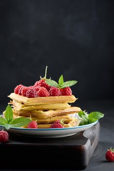 Stack of baked Belgian waffles with ripe red raspberry, green mint leaves 