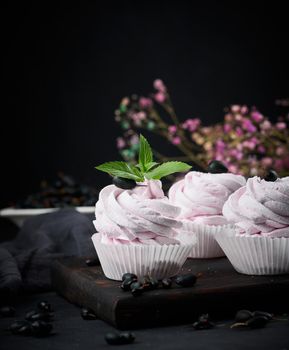 Portioned fruit marshmallows in a paper cup on a black wooden board, delicious dessert