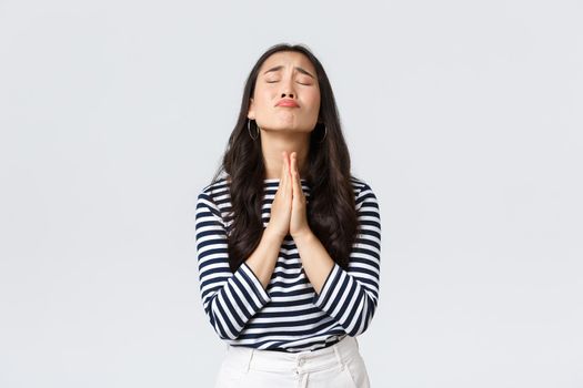 Lifestyle, people emotions and casual concept. Desperate hopeful asian girl making wish, close eyes and hold hands in pray, pleading god to have something, making wishful face, white background.