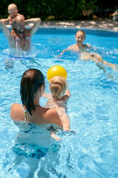 Parents with small kids playing with a ball in the pool. High quality photo