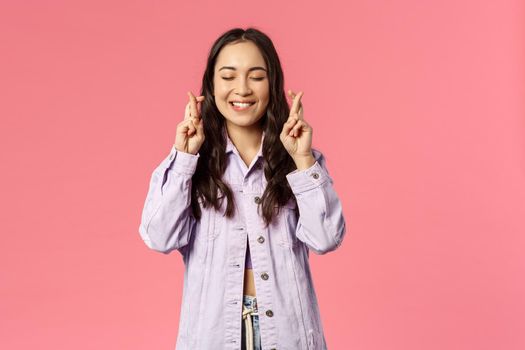 Hope my wish come true. Portrait of hopeful enthusiastic, attractive young asian girl praying, daydreaming with fingers crossed, beaming smile and closed eyes, want and plead for it.