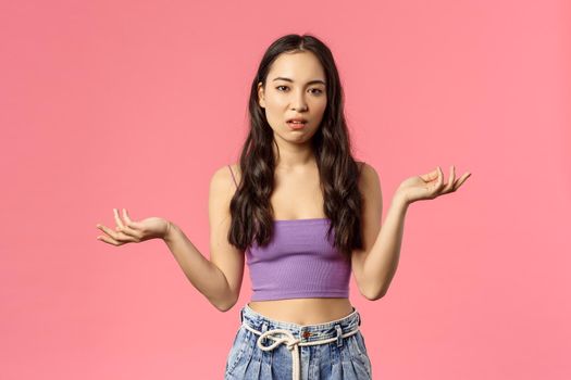 So what. Portrait of careless arrogant stylish asian girl shrugging, raise hands clueless and look camera with skeptical, unimpressed expression, dont care and not see any point, pink background.