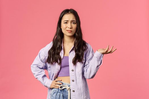 So what, I dont care. Portrait of skeptical, unimpressed and careless stylish girl, smirk unbothered shrugging and raise hand in dismay, listen to nonsense, standing pink background.