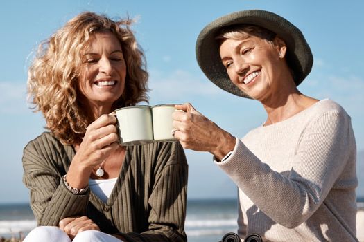Cheers to the good life. two attractive mature women enjoying some coffee while sitting on the beach