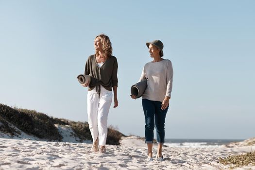 Taking the day to enjoy the beach. Full length shot of two attractive mature woman walking with their on the beach